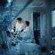 two medical workers assess lab microscope samples in a dimly lit lab