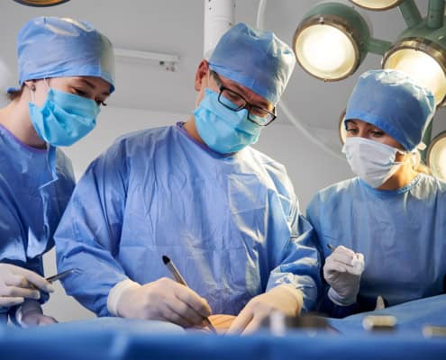Three doctors standing over a patient during surgery